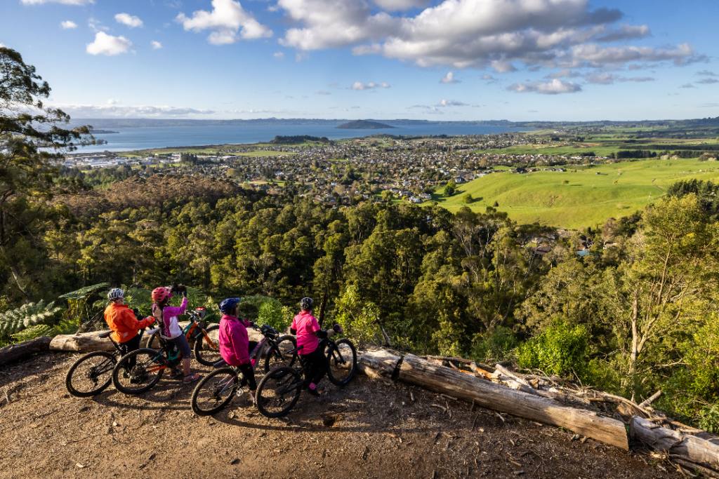 Cyclists stopped on the edge of a forest cliff looking down at fields